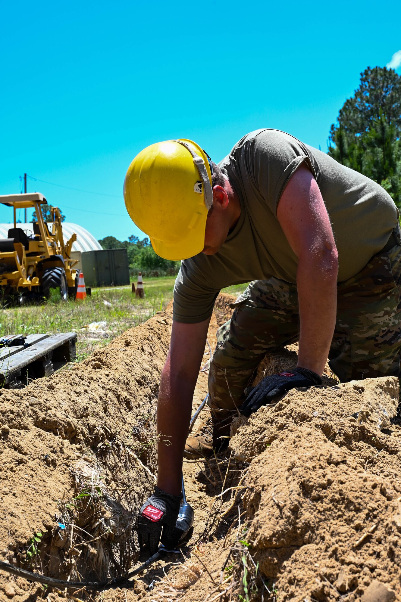 An Airman wearing military uniform lays fiber optic cable..