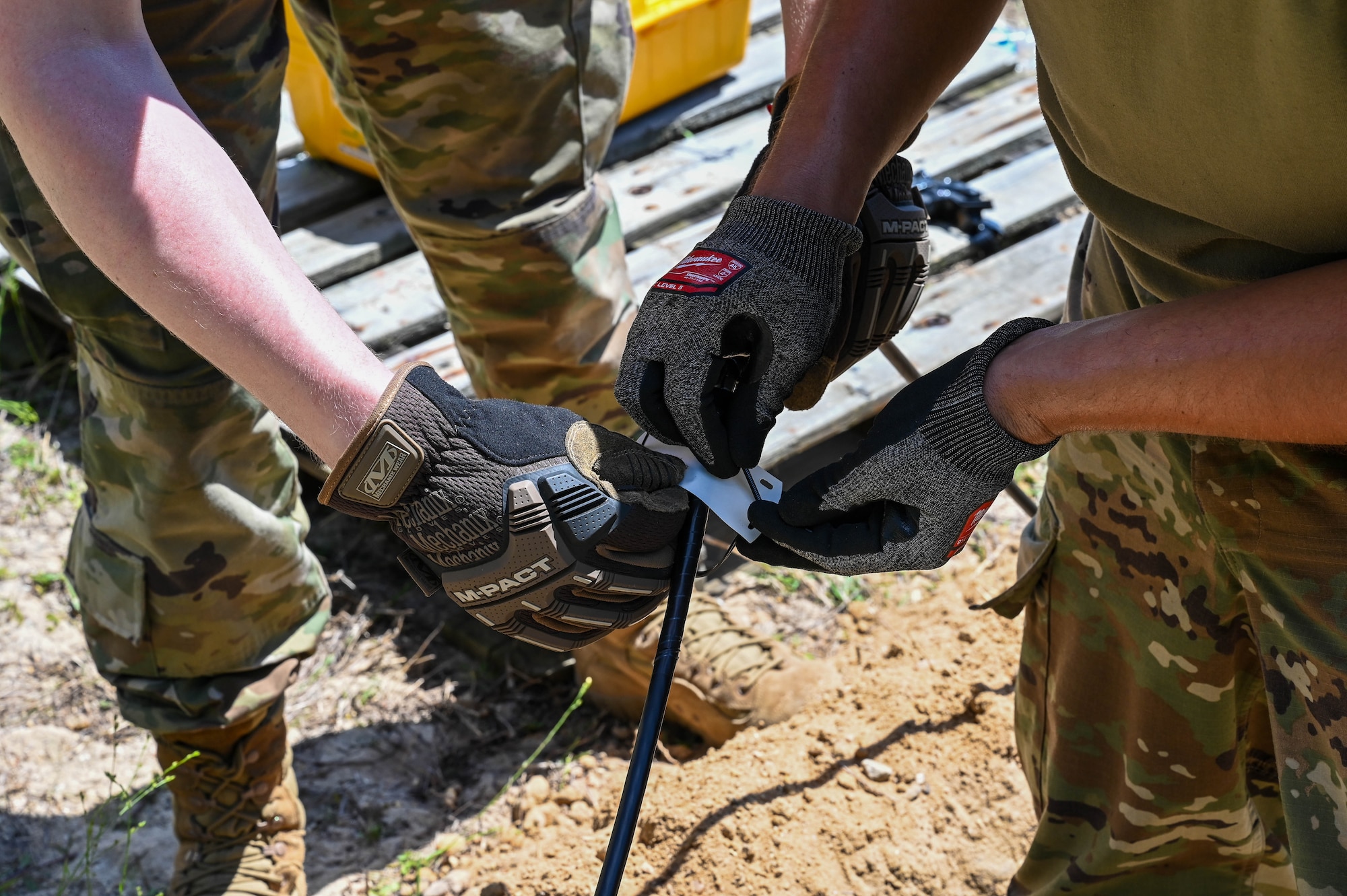 Two pairs of gloved hands placing a tag on a line of fiber optic cable during the hands-on scenario at the Expeditionary Communications Roundup.