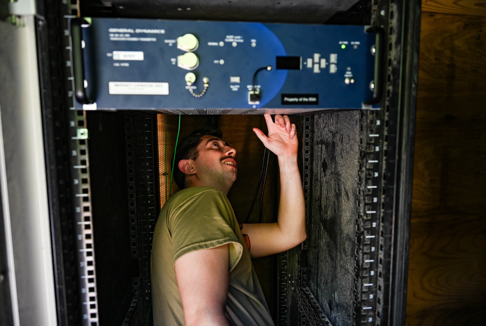An Airmen, wearing a military uniform, looks up at a communications receiver while standing under it