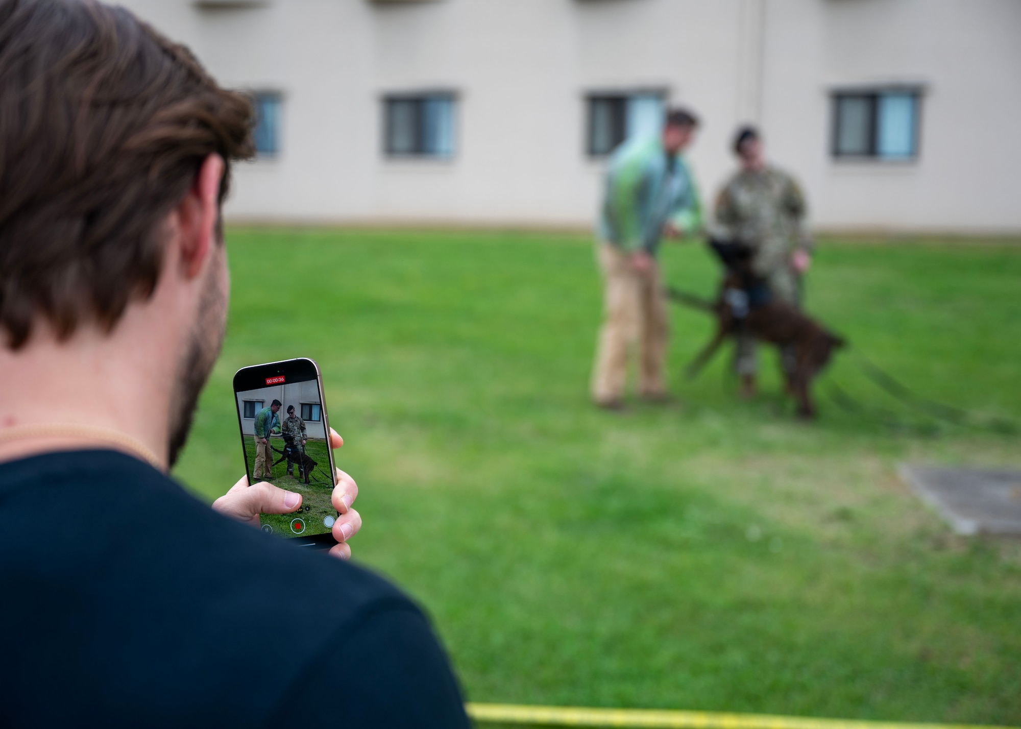 John K, singer, records a military working dog demonstration during a Law Enforcement Display in recognition of 2025 National Police Week at Osan Air Base, Republic of Korea, May 15, 2025. Military Working Dogs are a vital force multiplier, trained to detect threats, apprehend suspects, and protect service members with unwavering loyalty and precision. (U.S. Air Force photo by Senior Airman Sarah Williams)
