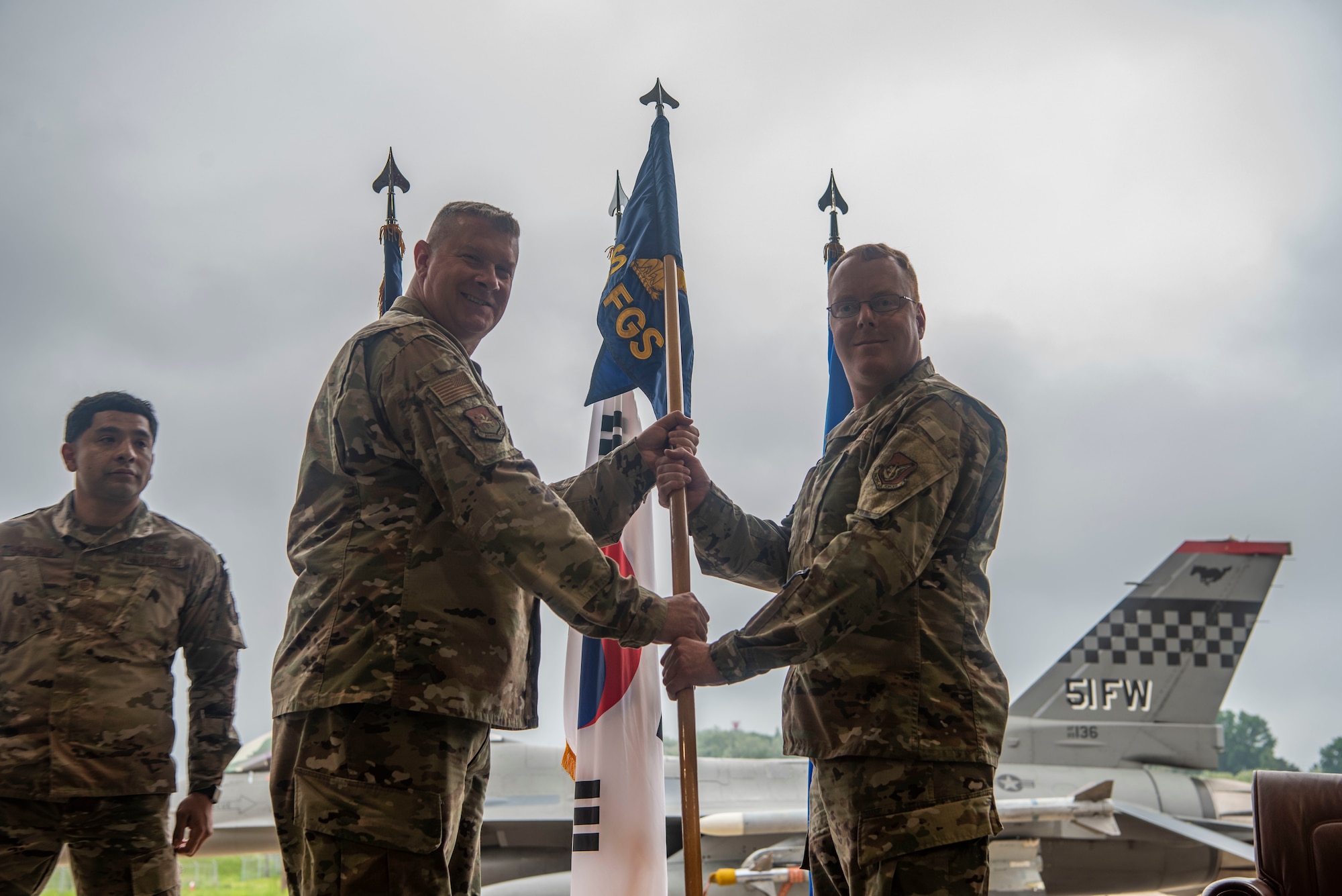 U.S. Air Force Maj. Richard Ryland, 36th Fighter Generation Squadron incoming commander, right, accepts the squadron guidon from Col. Kenneth B. Beebe III, 51st Maintenance Group commander, during the 36th FGS assumption of command ceremony at Osan Air Base, Republic of Korea, May 15, 2025.