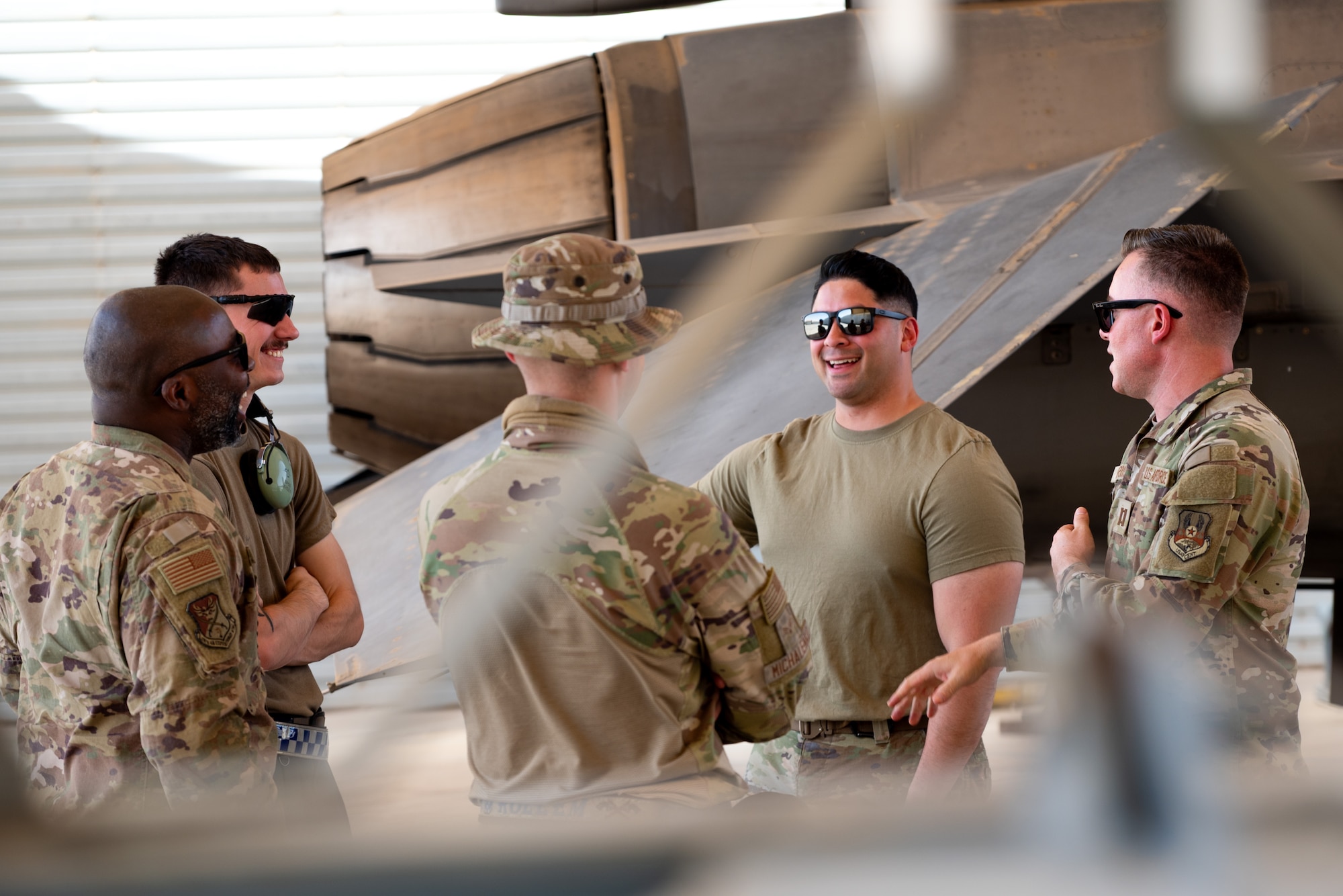 A group of 5 Airmen talk near the tail of an F-16 Aircraft
