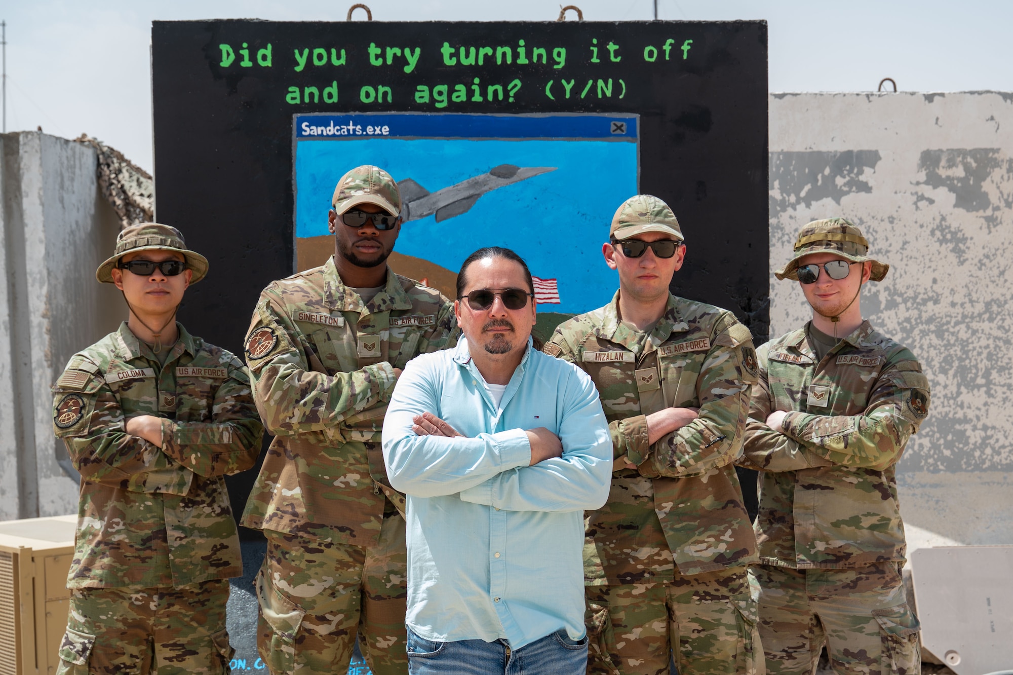 A group of Airmen and a contractor pose in front of a wall.