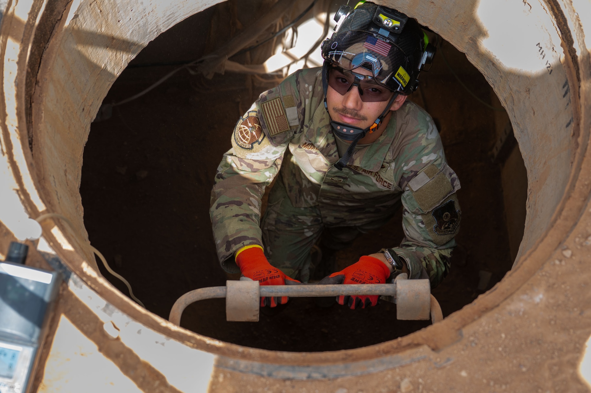 An Airman exits an underground manhole.