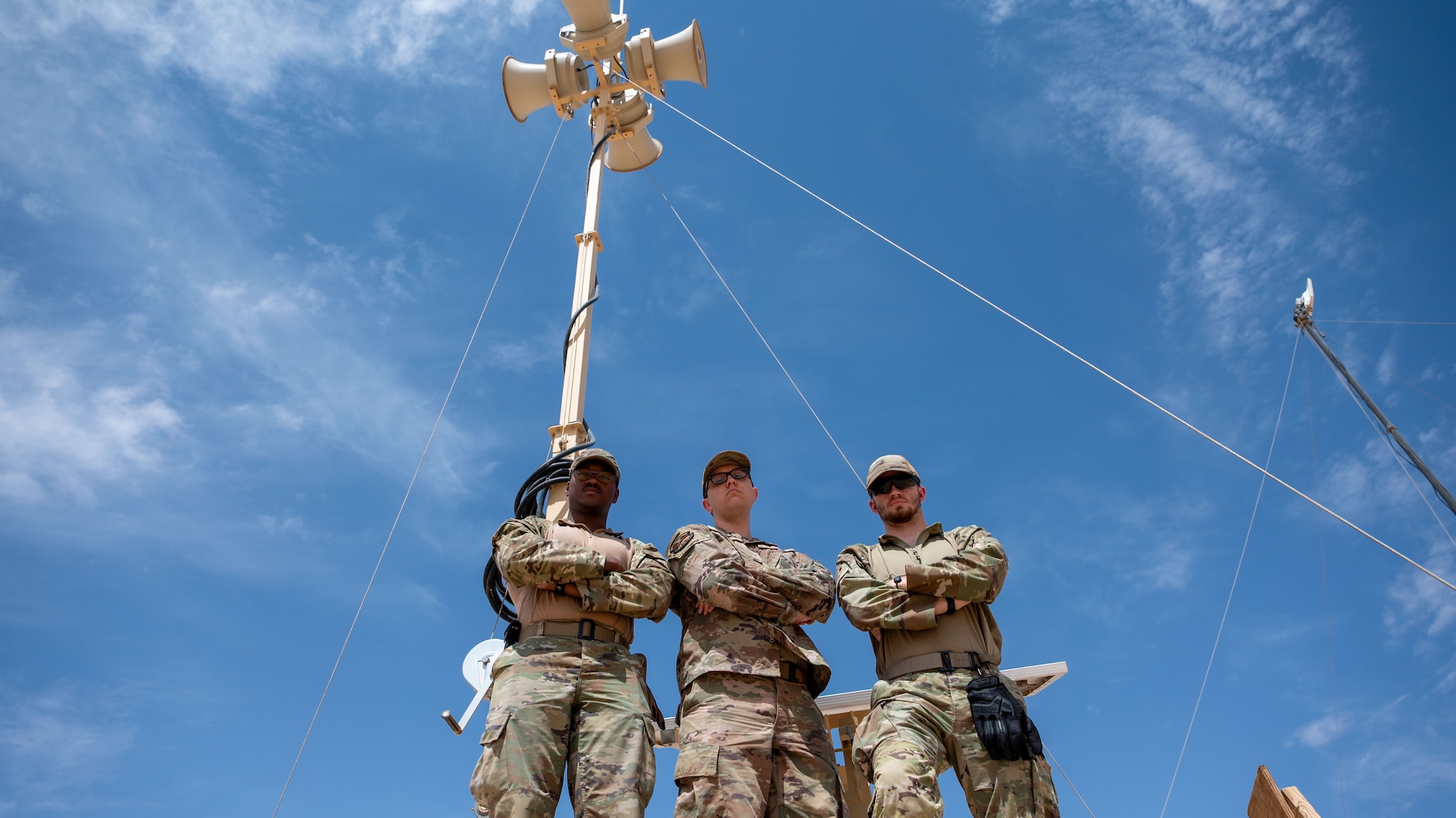 Three men pose for a photo in front of a radio speaker on a tall pole.