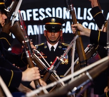 Army Soldiers dressed in dark ceremonial uniforms are performing a rifle drill routine while one Soldier walks up the middle of the formation.