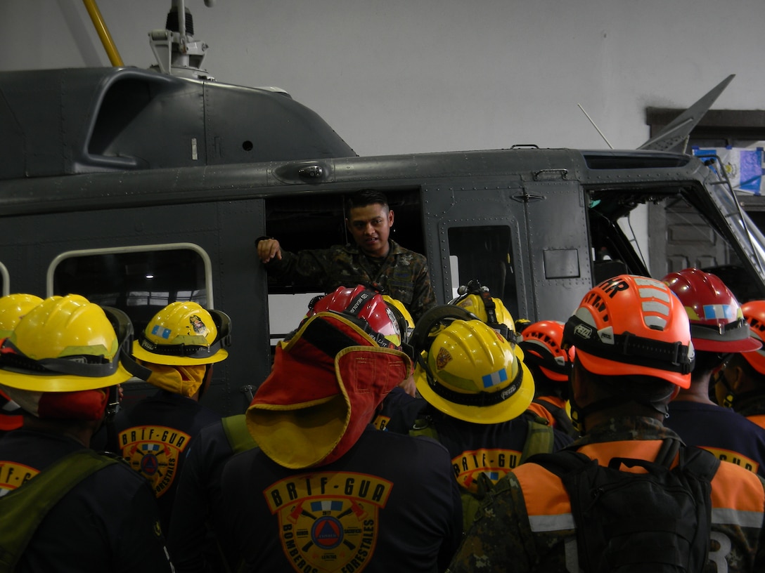 A Guatemalan soldier stands inside a helicopter while speaking to a group of firefighters.