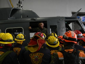 A Guatemalan soldier stands inside a helicopter while speaking to a group of firefighters.