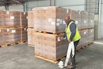 A man wearing a reflective safety vest places labels on a shipping pallet while standing in a warehouse.