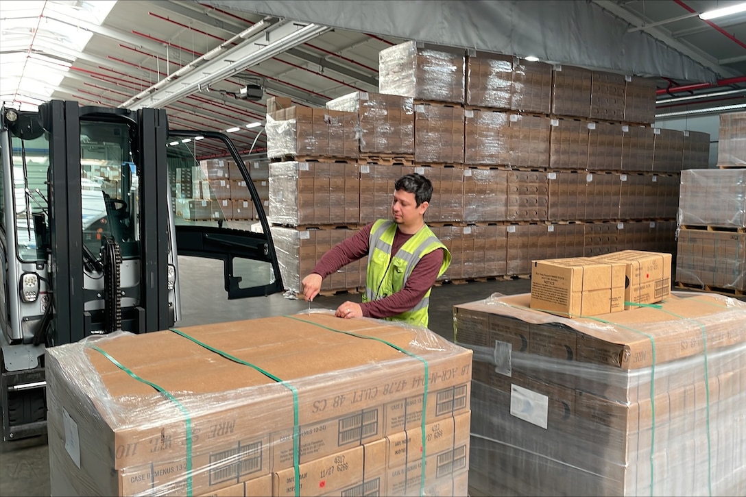 A man wearing a reflective safety vest places labels on a shipping pallet while standing in a warehouse.