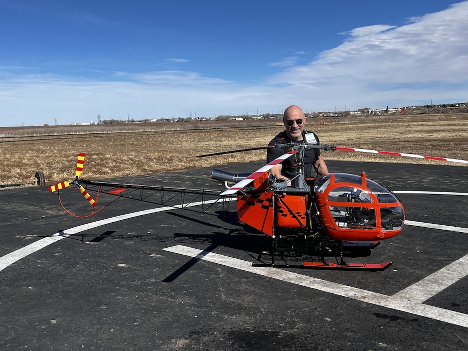 A gentleman kneels next to a red, scale, radio-controlled helicopter