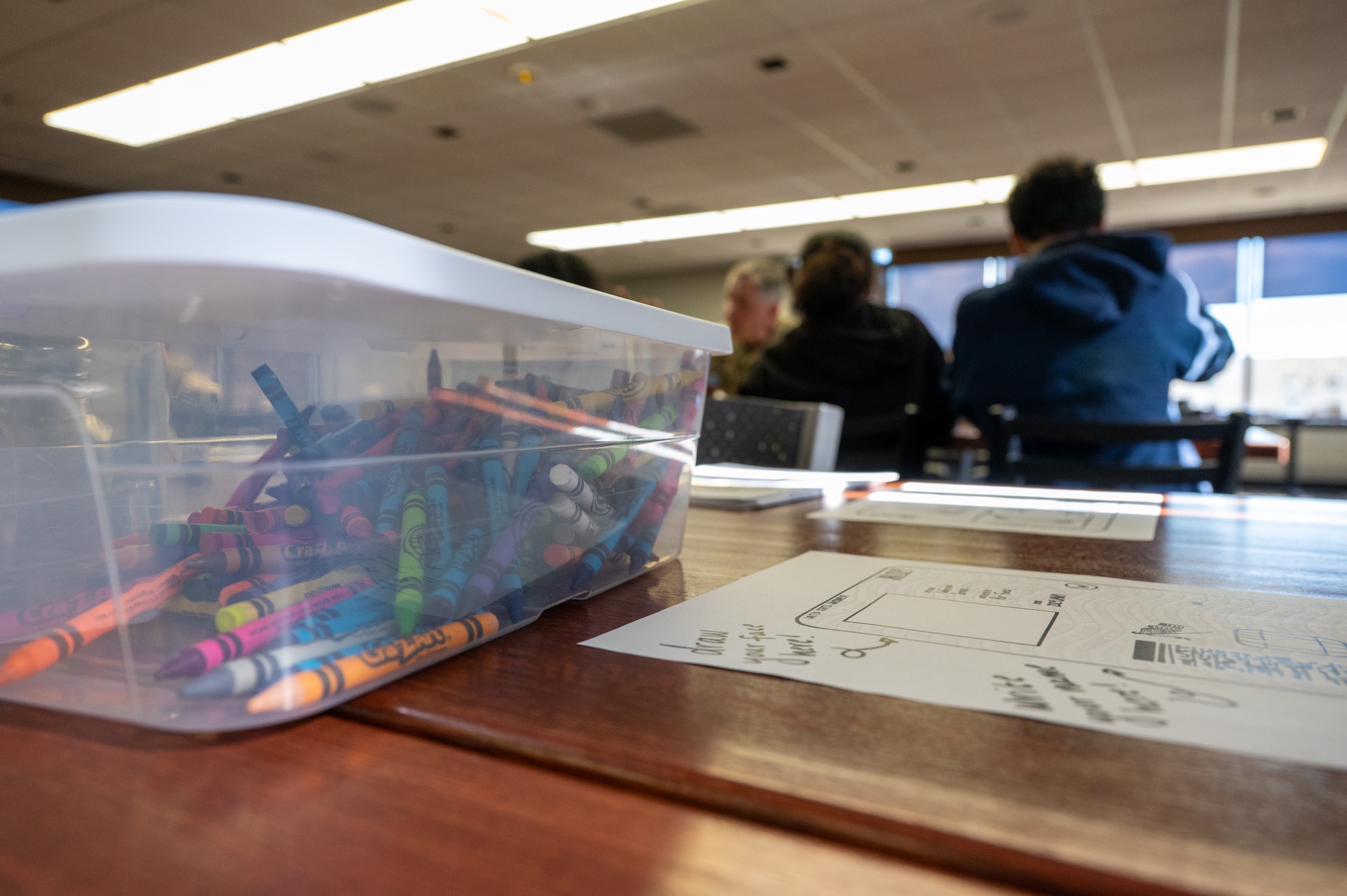 Coloring utensils and activities sit on a table with a military family in the background.
