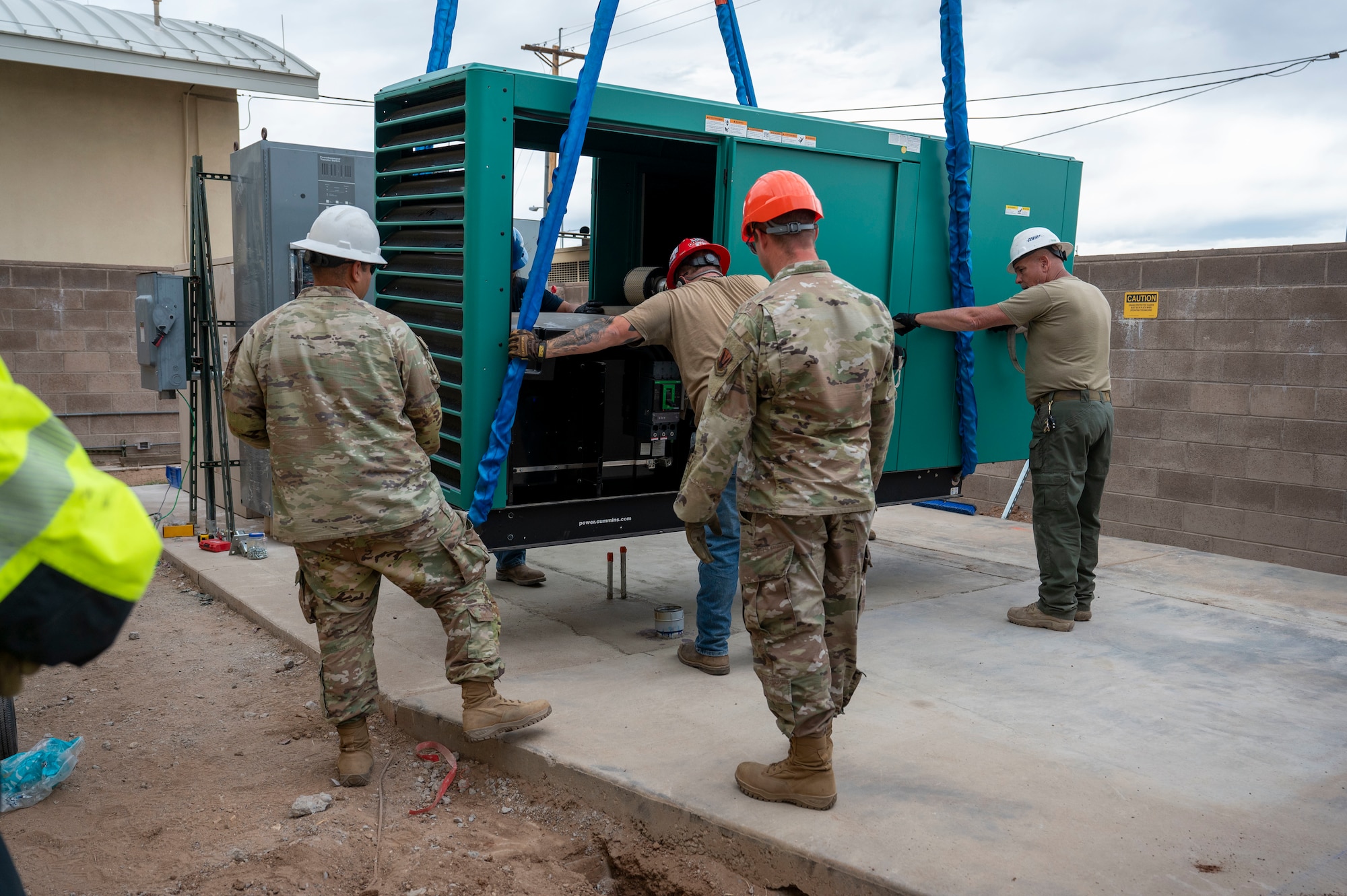 U.S. Airmen and civilians from the 355th Civil Engineer Squadron as well as Airmen from the Air Force Civil Engineer Maintenance Inspection and Repair Team and civilian contractors guide a new backup power generator into place at Davis-Monthan Air Force Base, Arizona, May 13, 2025.