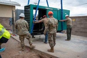 U.S. Airmen and civilians from the 355th Civil Engineer Squadron as well as Airmen from the Air Force Civil Engineer Maintenance Inspection and Repair Team and civilian contractors guide a new backup power generator into place at Davis-Monthan Air Force Base, Arizona, May 13, 2025.