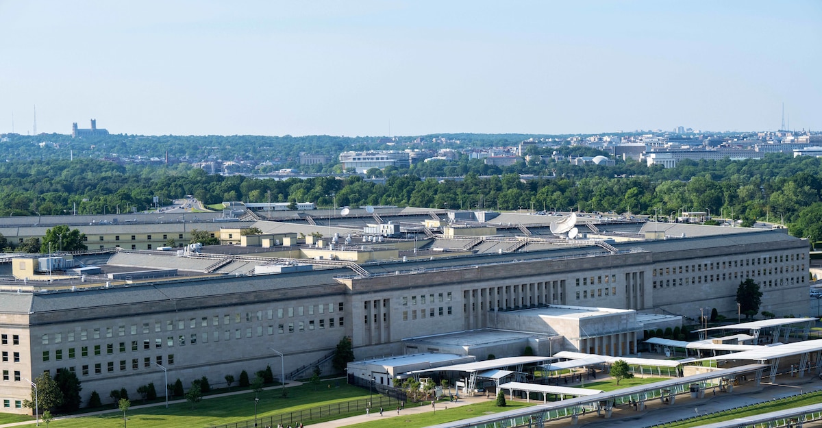 An aerial view of the Pentagon with trees and Washington, D.C. in the distant background.