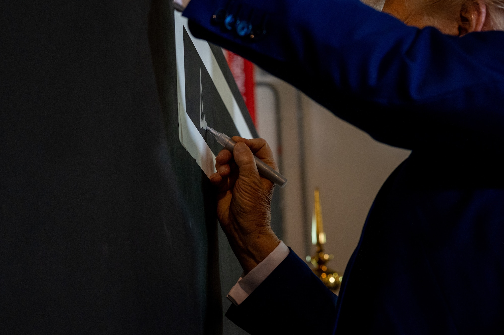 President Donald J. Trump signs a concrete T-Wall after meeting 379th Air Expeditionary Wing leadership, May 15, 2025. T-Walls, steel reinforced concrete blast walls, can be found throughout AUAB and squadrons often paint T-Walls to commemorate their deployments to AUAB. (U.S. Air Force photo by 1st Lt. Trevor Wood)