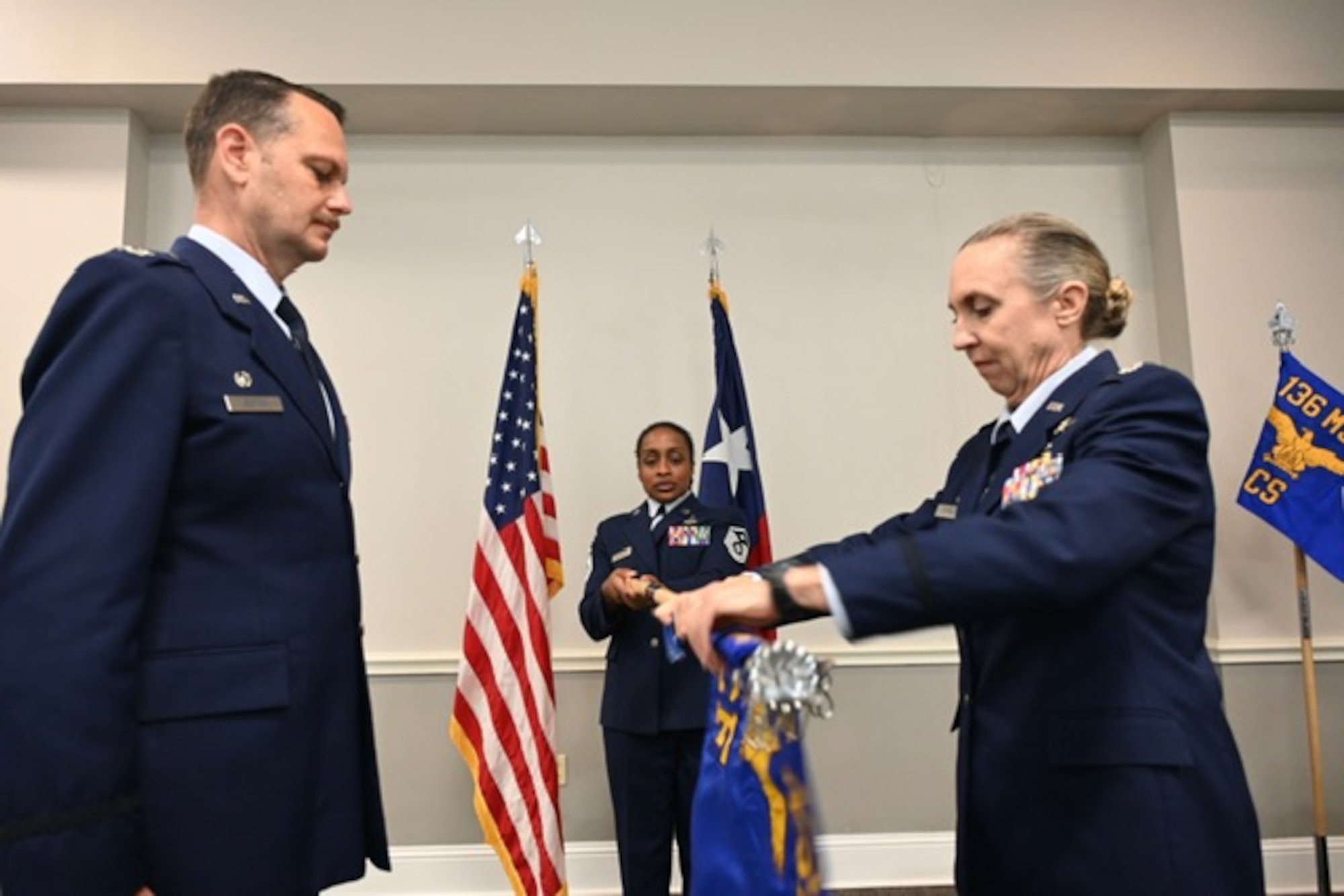 Texas Air National Guard Lt. Col Christine Wright, right, furls a guidon during a redesignation ceremony held at the 136th Airlift Wing Headquarters Building, Naval Air Station Joint Reserve Base, Fort Worth, Texas, May 17, 2025. The ceremony officially redesignated the 136th Communications Flight to the 136th Communications Squadron in order to better represent the unit's role in the wing. The new squadron guidon is visible in the back right of the photo. (Texas Air National Guard photo by Airman 1st Class Connor Dunne)