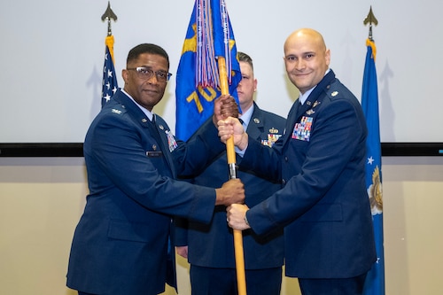 photo of three uniformed US Air Force Airmen standing on a stage, two holding a unit flag while one stands at attention behind them.