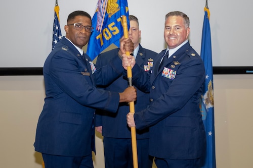 photo of three uniformed US Air Force Airmen standing on a stage, two holding a unit flag while one stands at attention behind them.