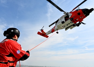 Helicopter with man on ground holding a line.