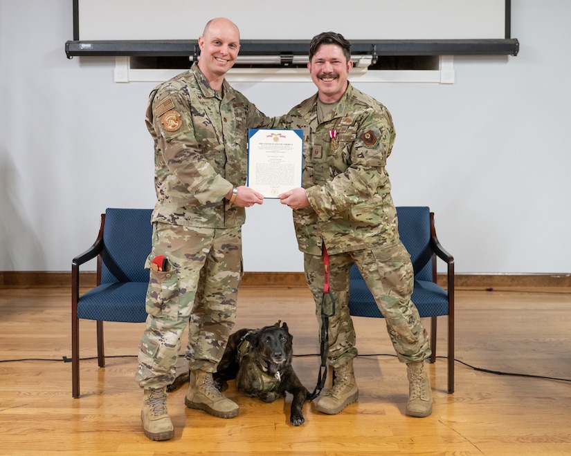 Master Sgt. Rudy Parsons, right, a pararescueman with the 123rd Special Tactics Squadron, is presented with a Meritorious Service Medal by Maj. Bryan Hunt, unit commander, during a ceremony Jan. 24, 2025, at the Kentucky Air National Guard Base in Louisville, Ky., to bid farewell to Parsons and Callie, center, the only certified rescue dog in the Department of Defense. Callie is retiring, and Parsons has been named pararescue career field manager for the Air National Guard.
