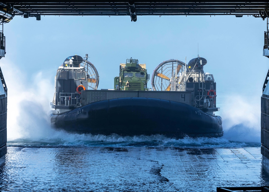 A boating vessel with a truck on its deck prepares to dock with a larger vessel in the ocean.