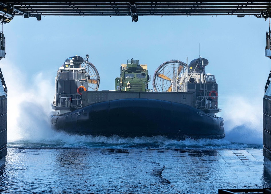 A boating vessel with a truck on its deck prepares to dock with a larger vessel in the ocean.