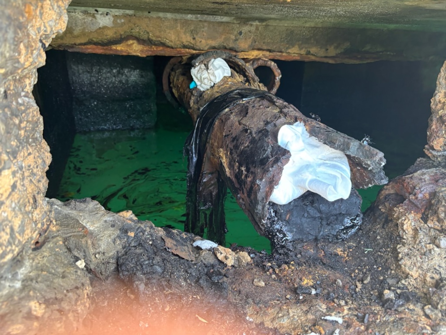 Photo of legacy pipe discharging oil, stuffed with absorbent boom, between Piers 2 and 3 in San Juan Harbor, Puerto Rico.  Coast Guard. Since April 11, 2025, Coast Guard Sector San Juan’s Incident Management team is investigating, responding and working with contracted oil spill removal organizations and local government authorities to contain and mitigate the pollution threat and clean up any recoverable product.  (U.S. Coast Guard photo)