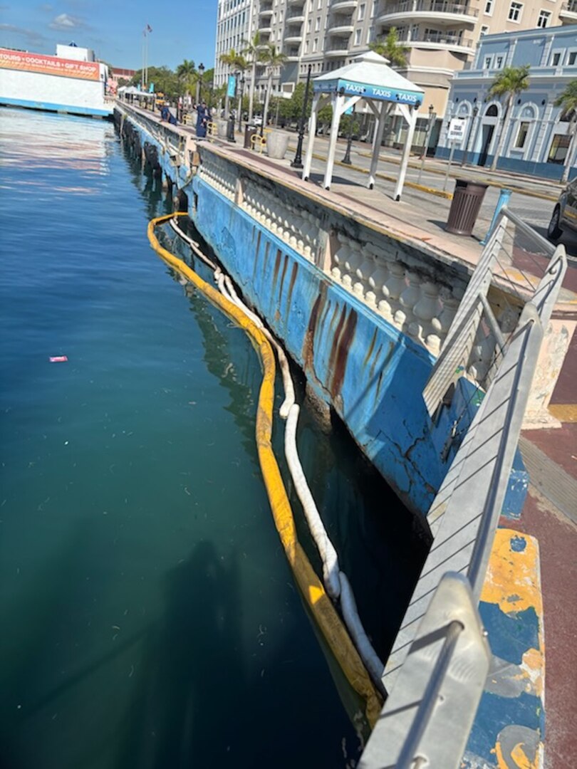 Photo showing containment and absorbent booms deployed in clean-up site for a legacy pipe discharging oil between Piers 2 and 3 in San Juan Harbor, Puerto Rico. Since April 11, 2025, Coast Guard Sector San Juan’s Incident Management team is investigating, responding and working with contracted oil spill removal organizations and local government authorities to contain and mitigate the pollution threat and clean up any recoverable product.  (U.S. Coast Guard photo)
