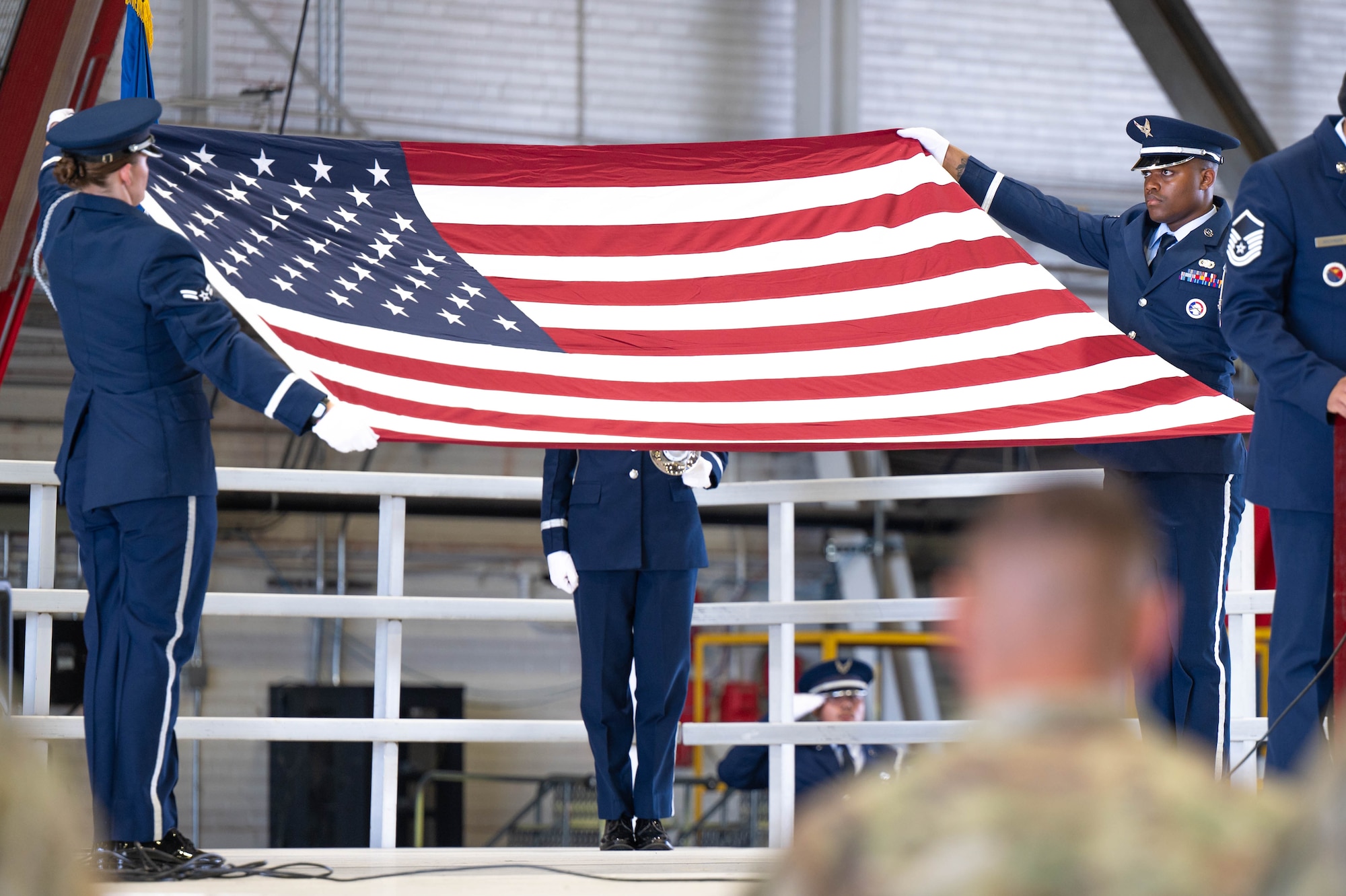 Four Airmen stand on stage during a Police Week ceremony at Scott Air Force Base. One Airman stands at a podium while three honor guardsmen perform Taps; two of them hold a fully extended American flag.
