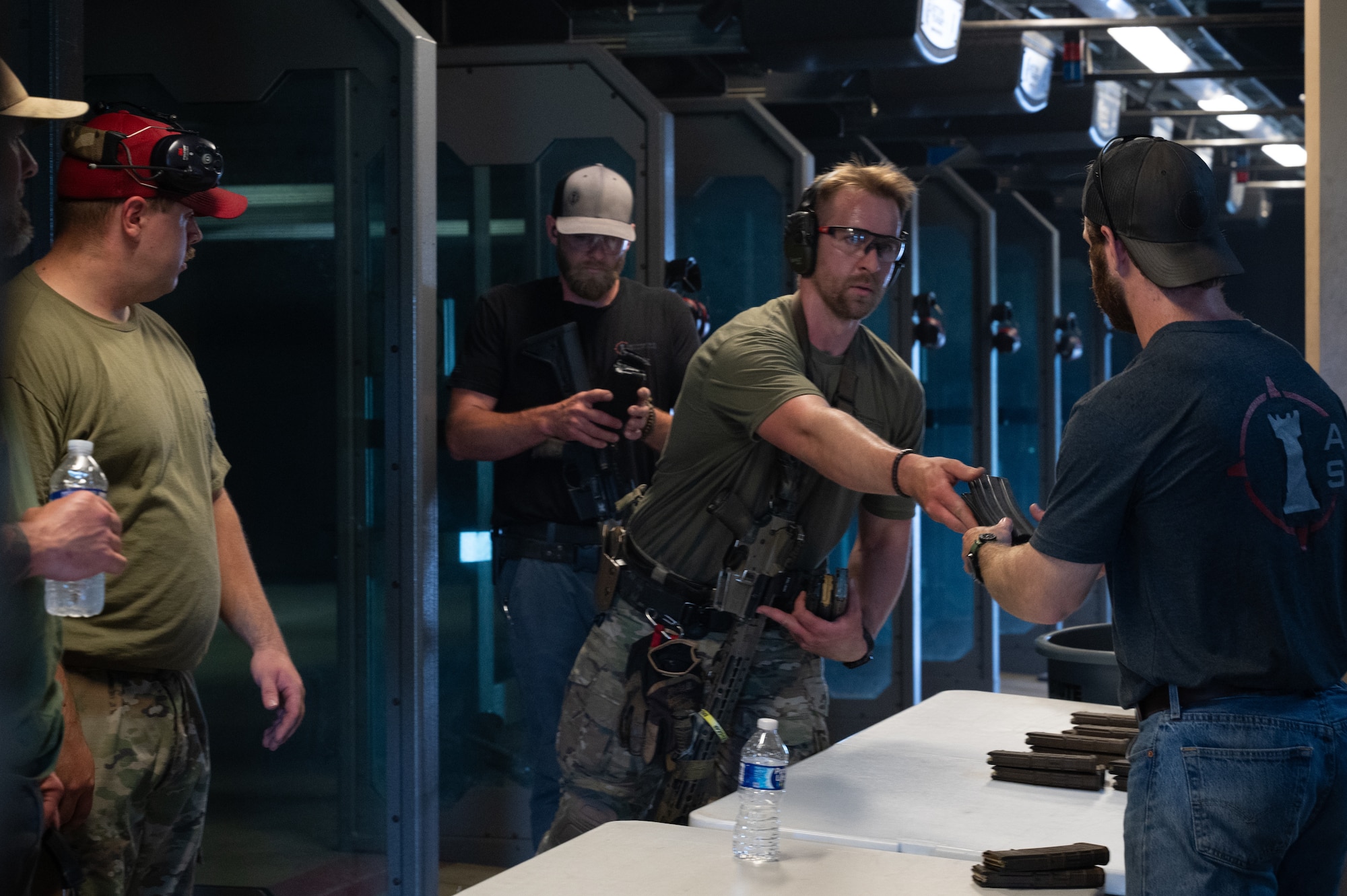 An Airman and a civilian complete a high-intensity marksmanship challenge during Police Week at Scott Air Force Base. The Airman, wearing protective eye gear, reaches over to hand an empty magazine to the civilian assisting.