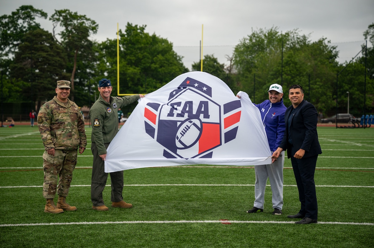Four people pose for a photo holding a white flag that says "FAA" in blue letters