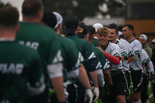 Photo shows a line of people wearing green jerseys shaking hands with another line of people wearing white jerseys following an American football game