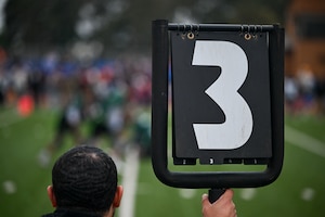 A man holds an American football down marker showing the number three. Signaling third down during a game