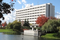 A white building stands on landscaped grounds behind a body of water.