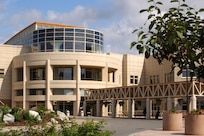 A building with a curved exterior stands on a landscaped lot.