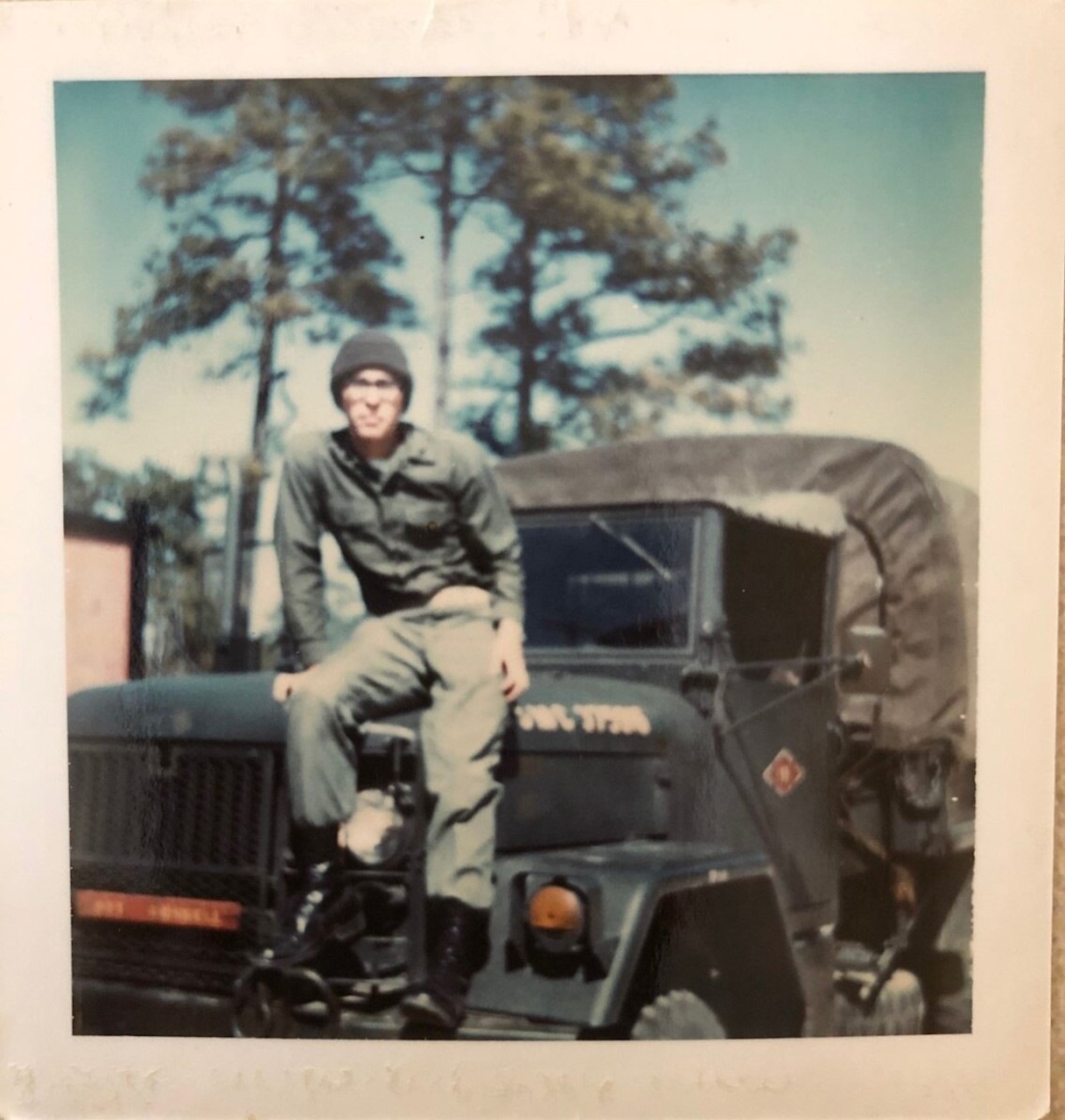 A Marine sits on the hood of his military truck.