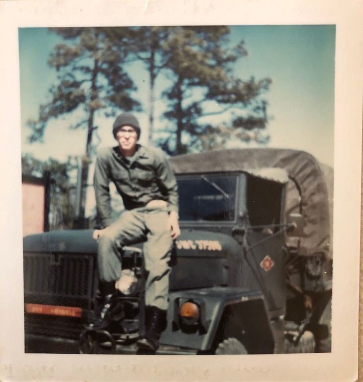 A Marine sits on the hood of his military truck.