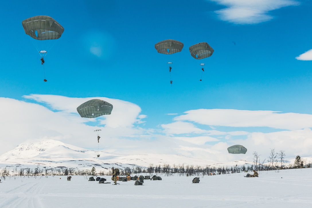 Five parachutes descend toward snow-covered ground in a vivid blue sky.