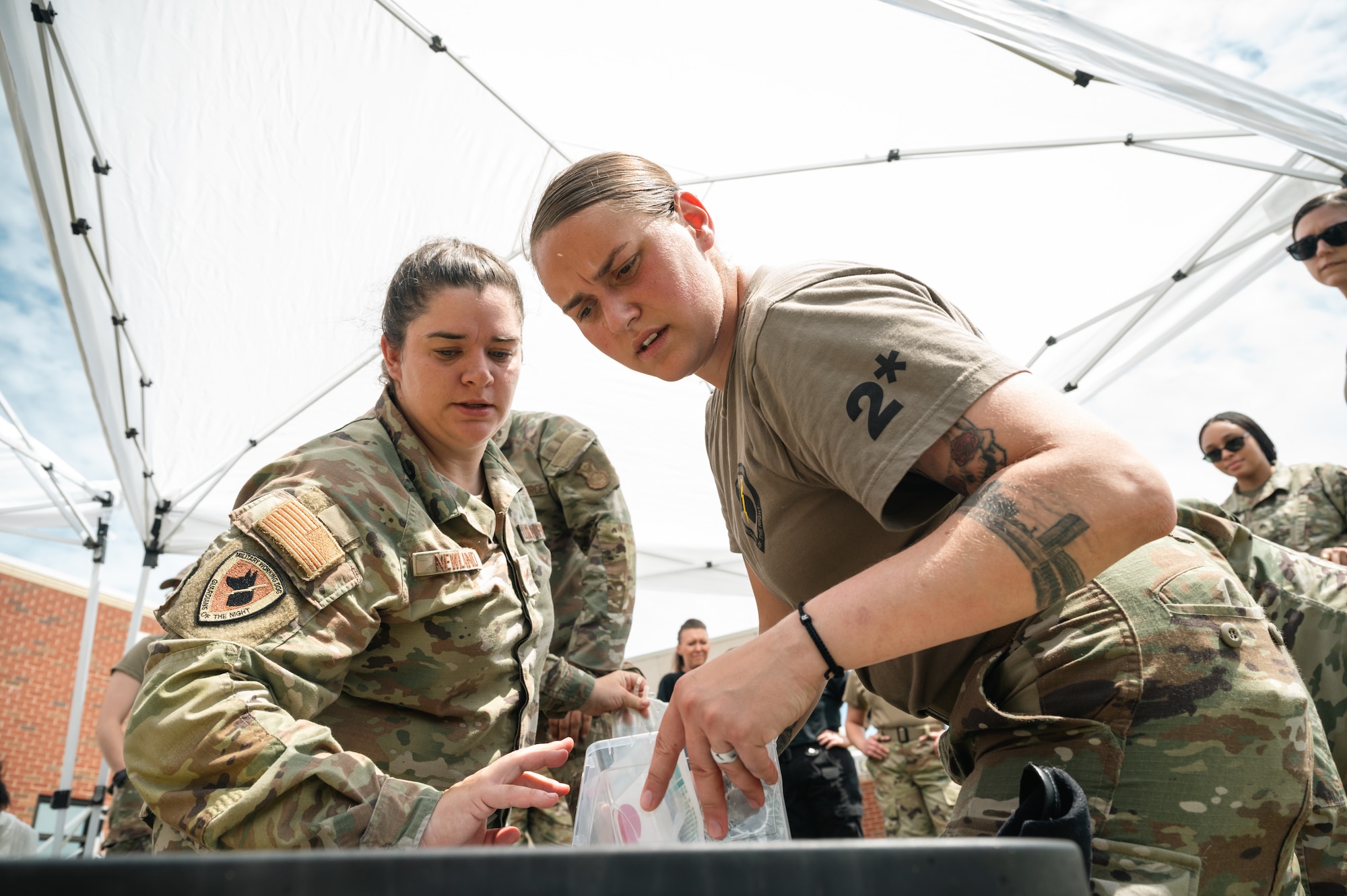 Two women in uniform reach into a tote outside
