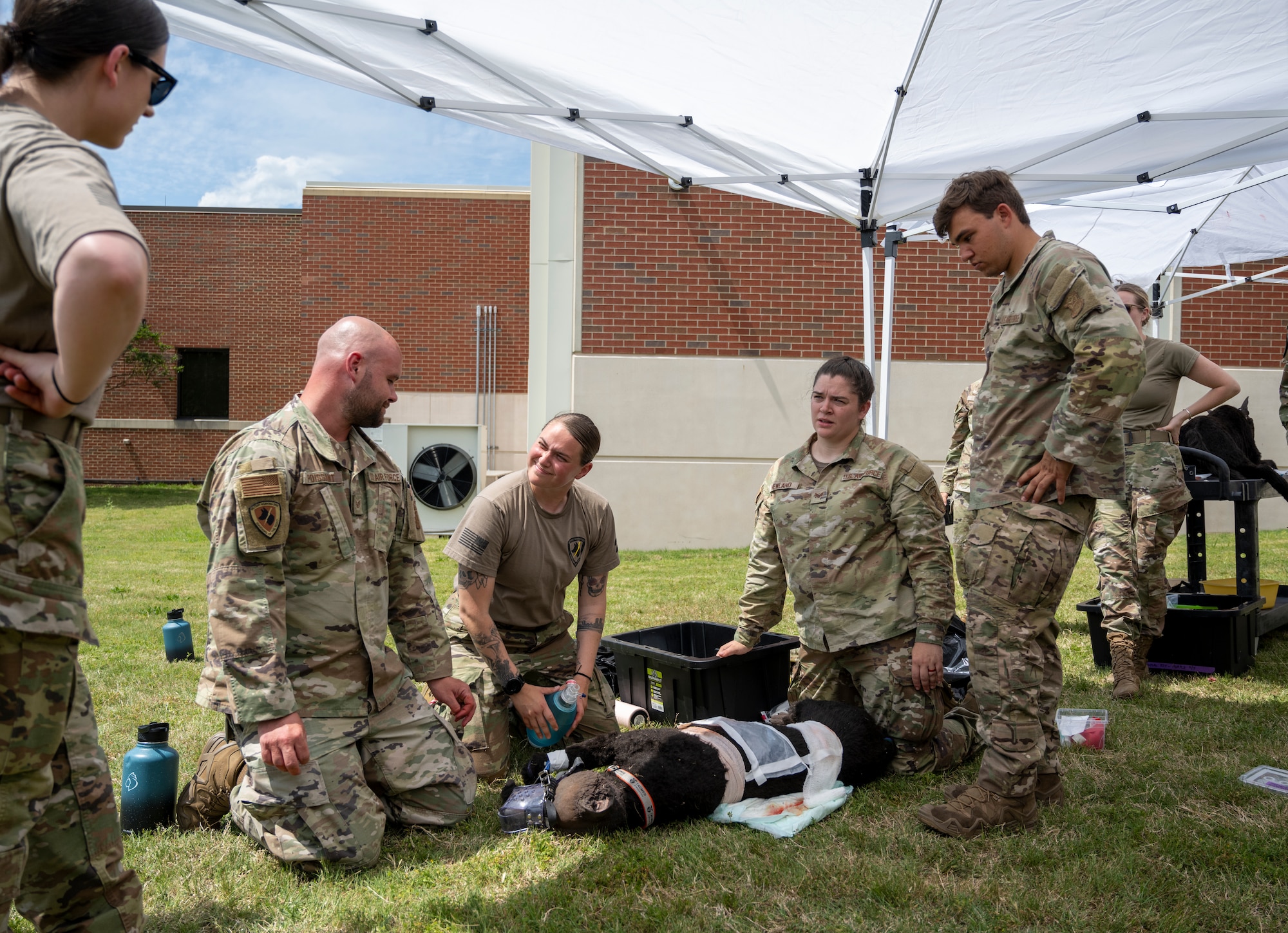 Four Airmen look at each other while kneeling in the grass.