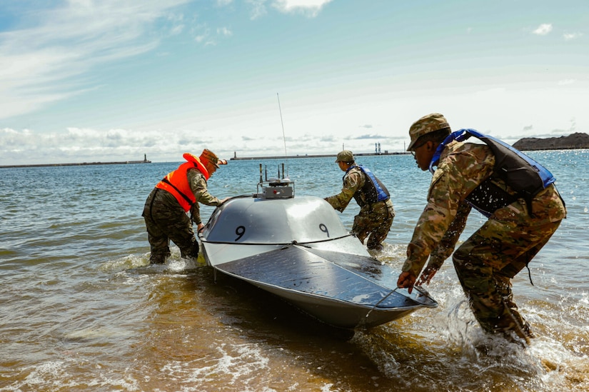 Three men in uniform pull a small unmmanned boat out of the water.