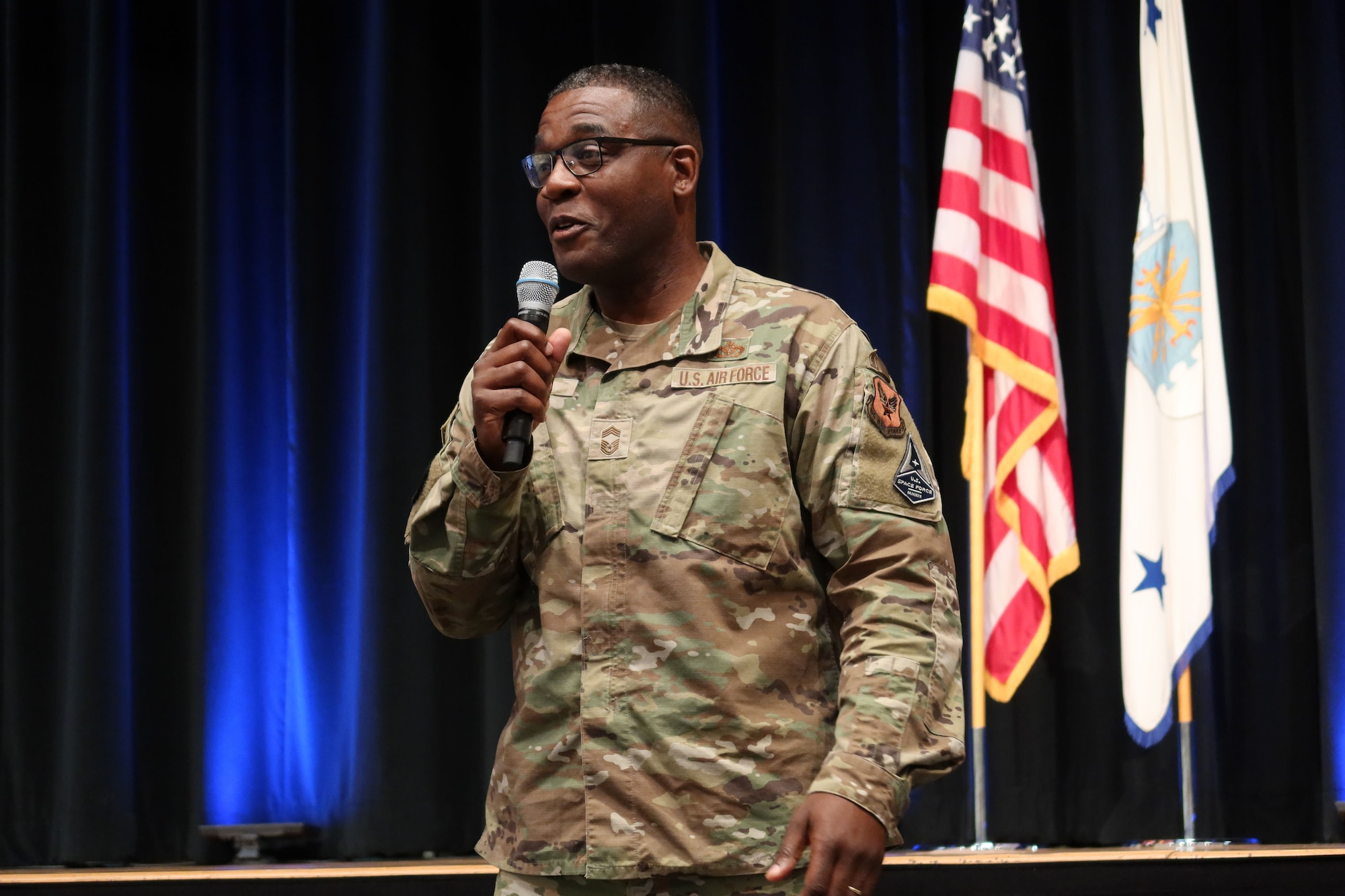 Chief Master Sgt. Wendell Snider holds microphone while addressing staff during Q2 All Call