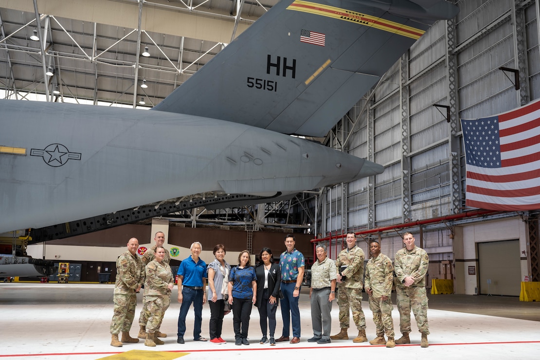 U.S. Air Force Airmen and honorary commanders pose for a group photo under the tail of a aircraft.