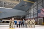 U.S. Air Force Airmen and honorary commanders pose for a group photo under the tail of a aircraft.