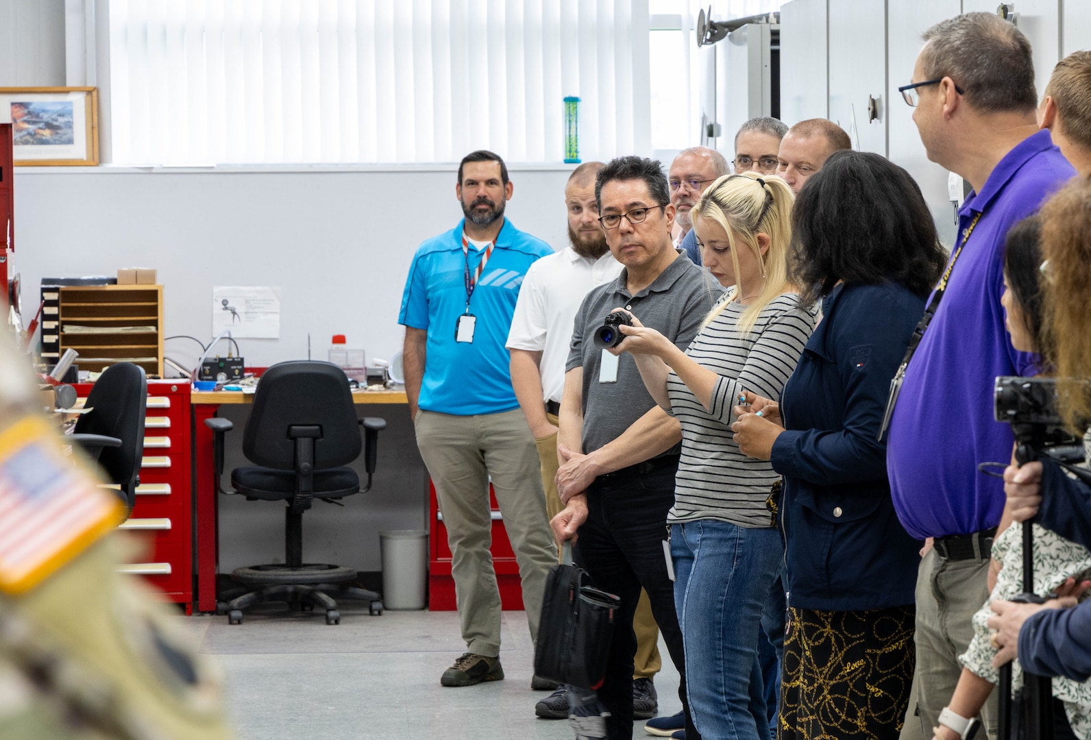 A blonde woman with gray and black striped shirt examines a small piece of equipment while others stand by.