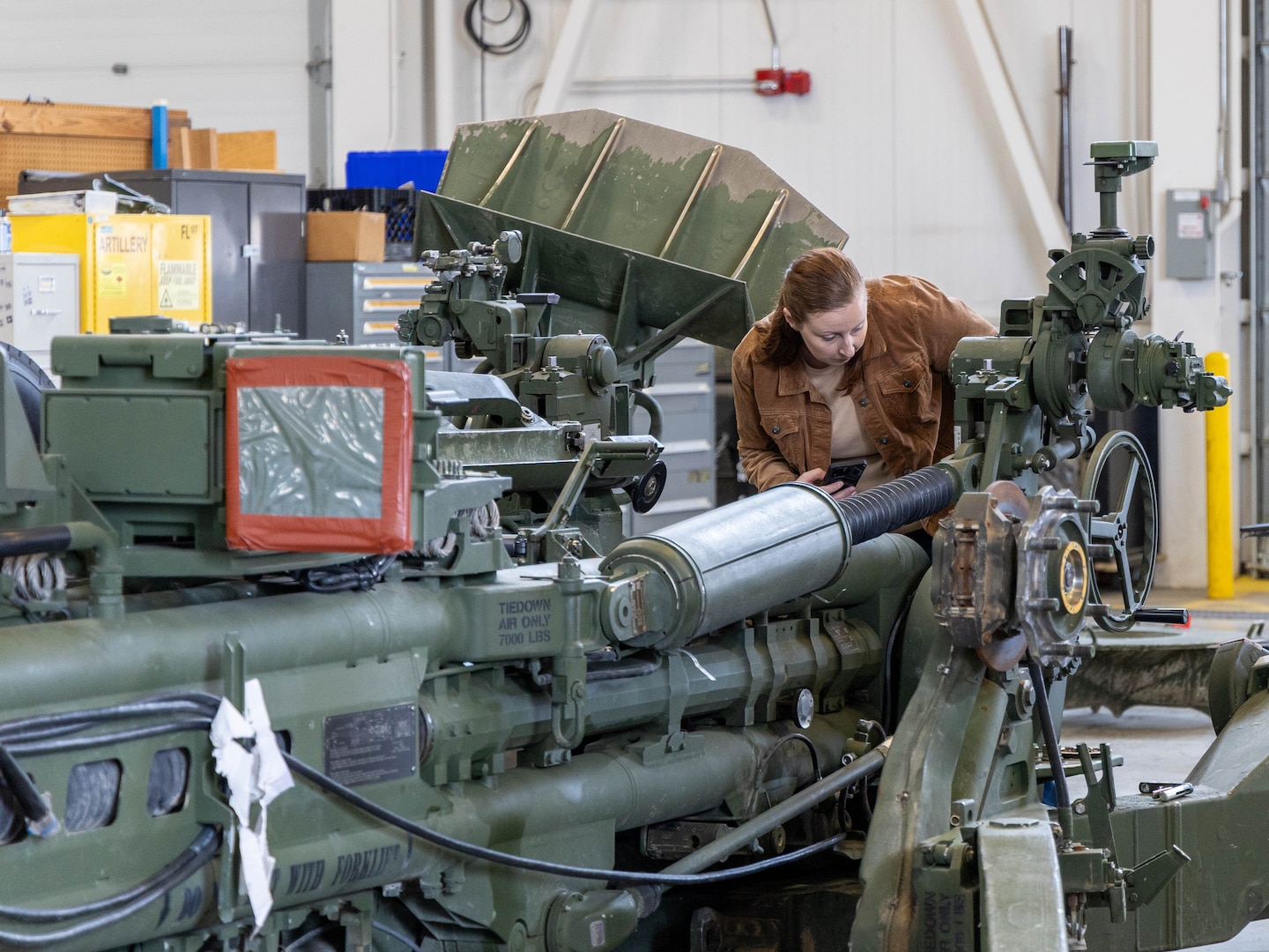 Woman wearing brown shirt examines a large, green military weapon system.