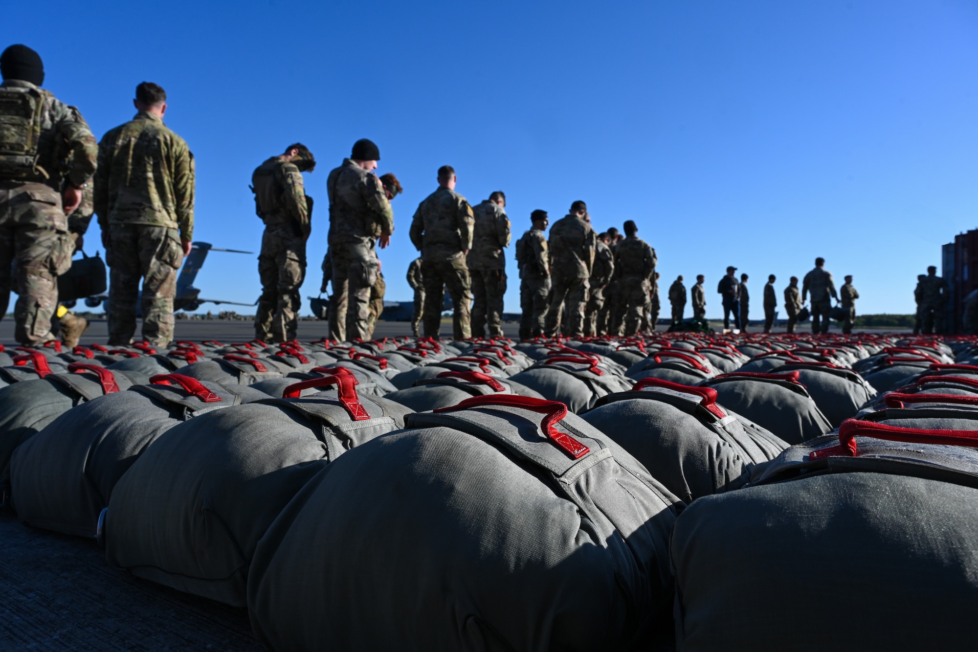 U.S. Army paratroopers from the 173rd Airborne Brigade stand in line as they grab their parachutes before a jump during Swift Response 25 on the flightline at Spangdahlem Air Base, Germany, May 16, 2025.