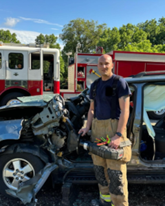 Defense Logistics Agency Land and Maritime Firefighter and Paramedic Donald Bruschi stands next to a vehicle holding an extrication device
