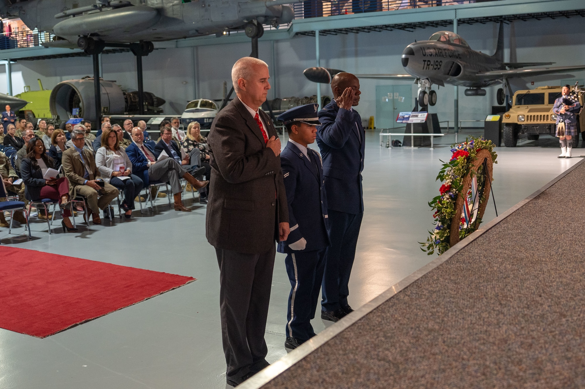 Three men standing in front of a wreath while man on the right salutes it